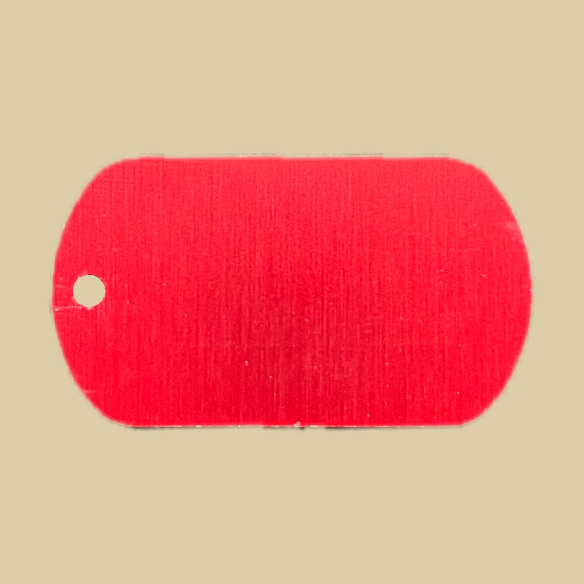 A single blank red medical alert tag on a plain khaki backdrop. The face is a bright anodized red with a fine vertical brushed grain, and there is a bead chain hole at the left end.